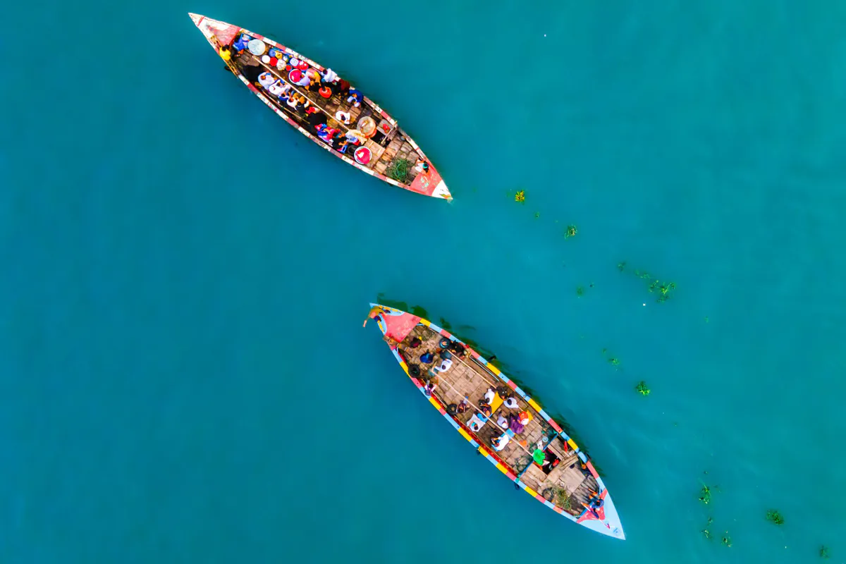 Two long wooden boats carrying passengers and goods on turquoise water, seen from directly above